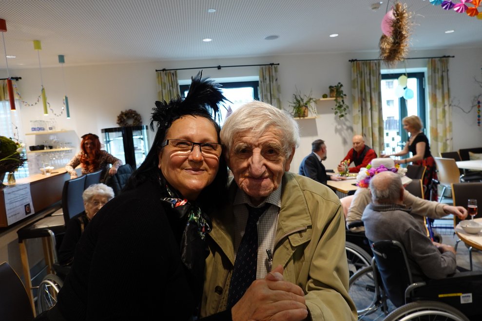Bewohner mit Mitarbeiterin lächeln in die Kamera.