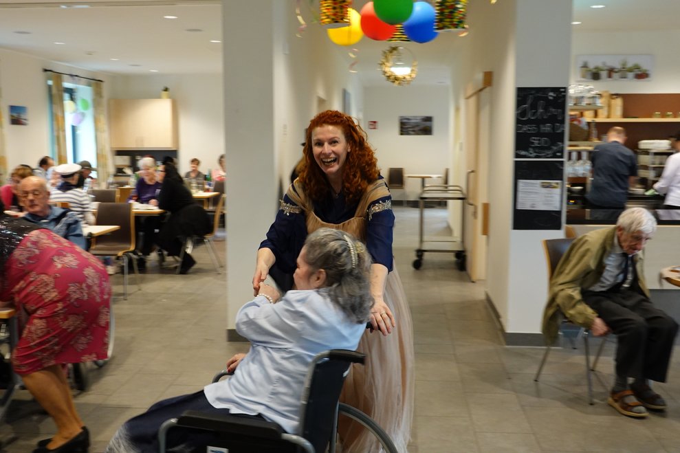 Mitarbeiterin und Bewohnerin im Rollstuhl tanzen miteinander.