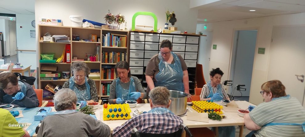 Bewohnerinnen und Bewohner färben mit ehrenamtlicher Mitarbeiterin Eier