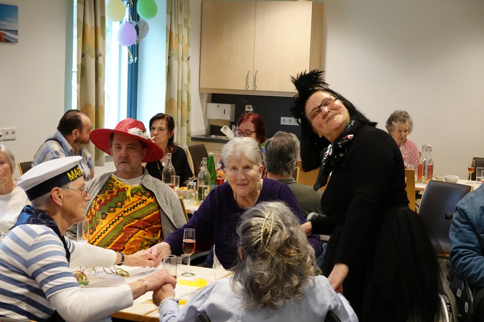 Mitarbeiterinnen, Ehrenamtliche und Bewohnerinnen schunkeln gemeinsam am Tisch.