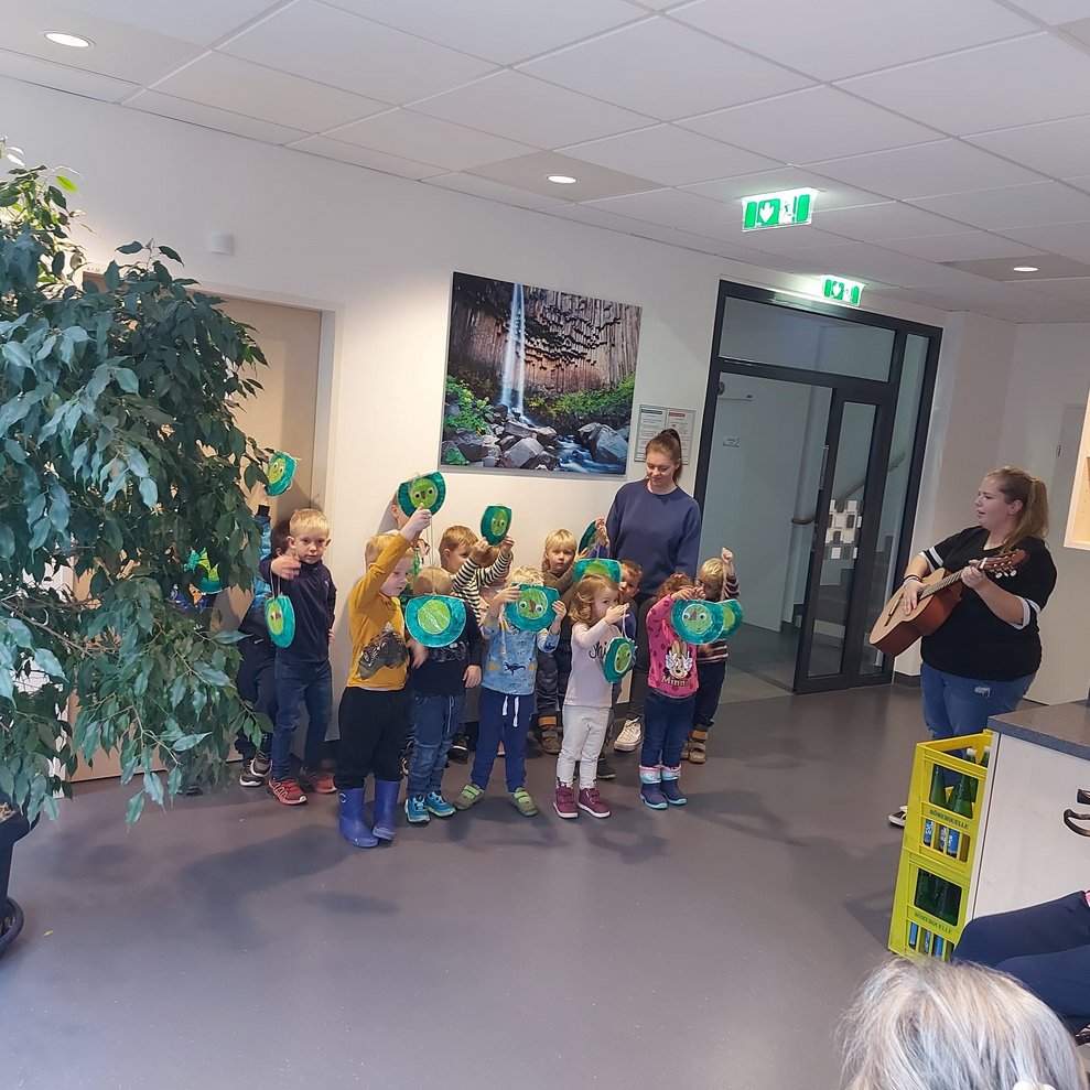 Kinder singen, Kindergartenbetreuerin spielt Gitarre